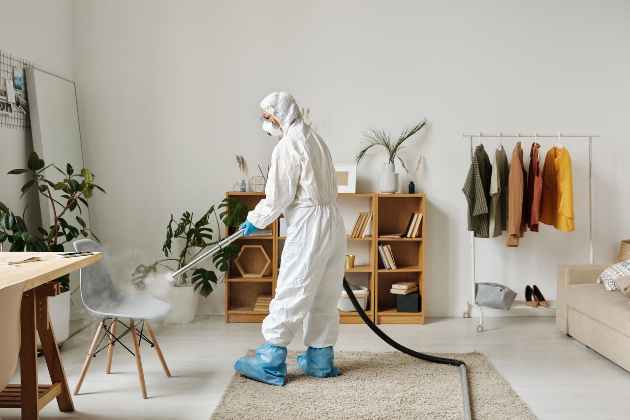 gallery-03 A technician wearing protective equipment sanitizing a contemporary living room with a fogging machine.